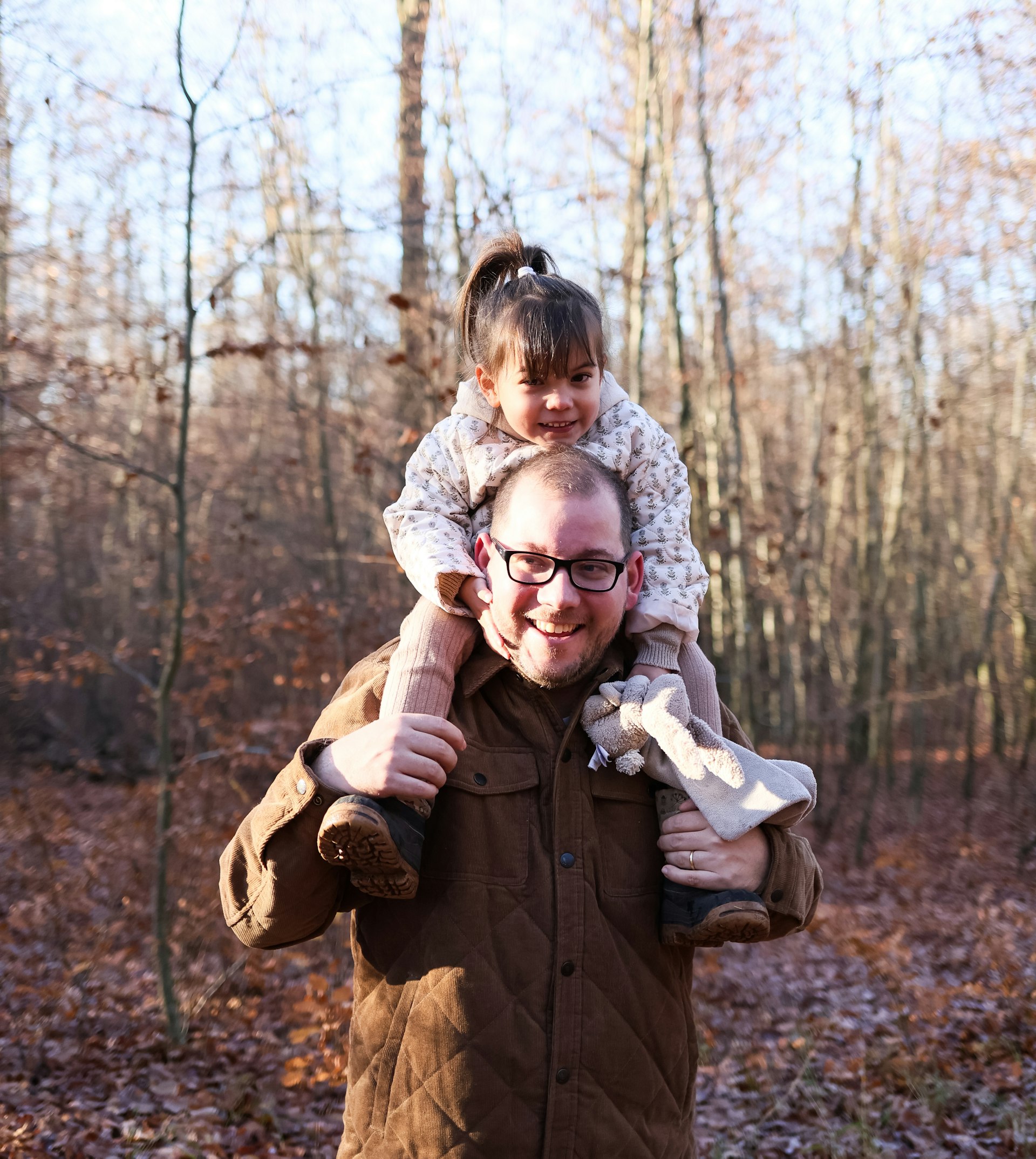 A father carrying his daughter on his shoulders in autumn woods